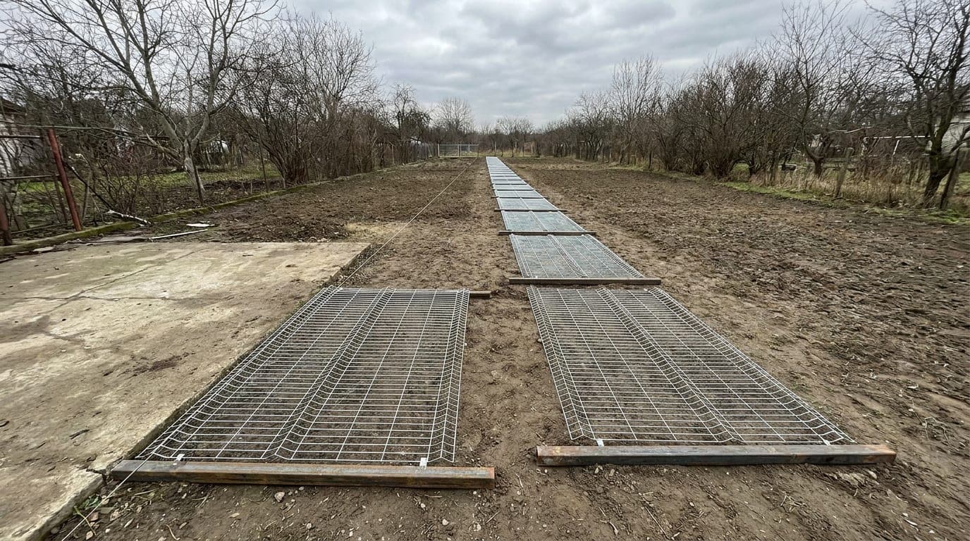 Çit güzergâhı boyunca kazıklarla işaretlenmiş bir kenar, kenarın sonunda duran kapı açıklığı ve yere dizilmiş galvanizli panel çit levhaları